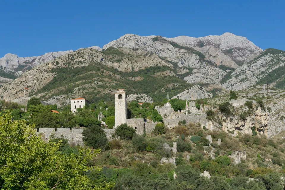 Ruined stone houses and a clock tower of Stari Bar rising beneath rocky Rumija mountain
