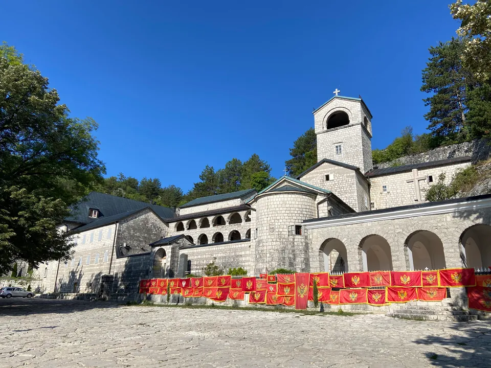 Cetinje Monastery building with its bell tower and Montenegrin flags hung along the fence.