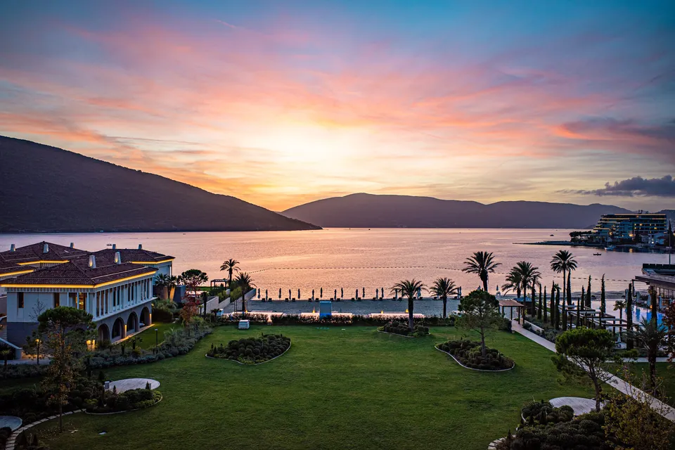 Sunset over the Portonovi resort with palm trees, a private beach and the bay beyond