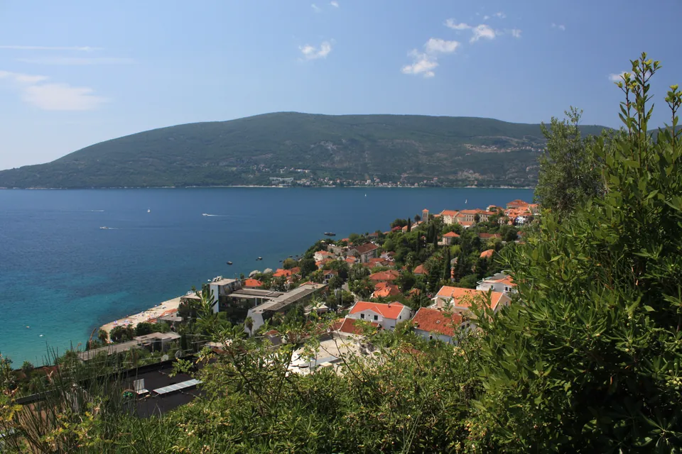 Panoramic view of Herceg Novi's coastline and the Bay of Kotor beneath a green hillside
