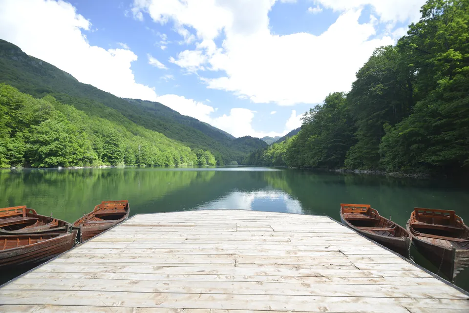 Wooden jetty with rowboats on Biograd Lake, forested slopes reflected in calm green water