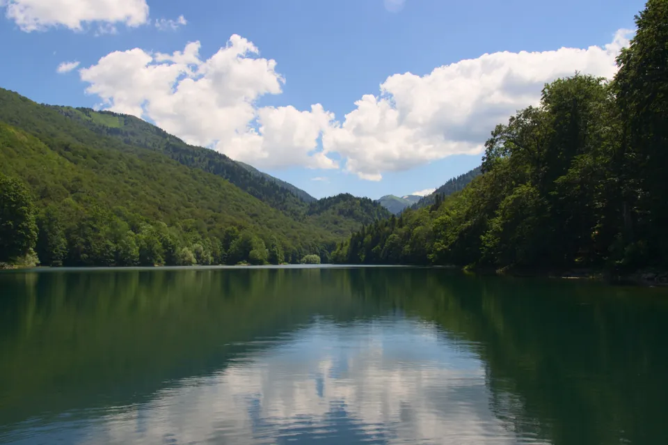 Still forest-ringed waters of Biograd Lake under a partly cloudy summer sky