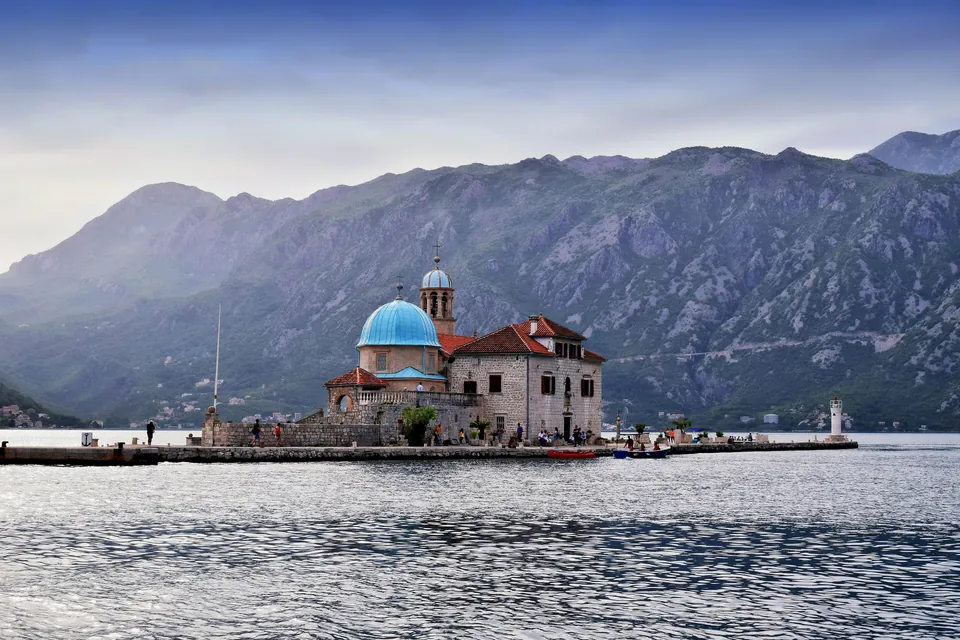 Church of Our Lady of the Rocks with a blue dome on an islet, mountains behind