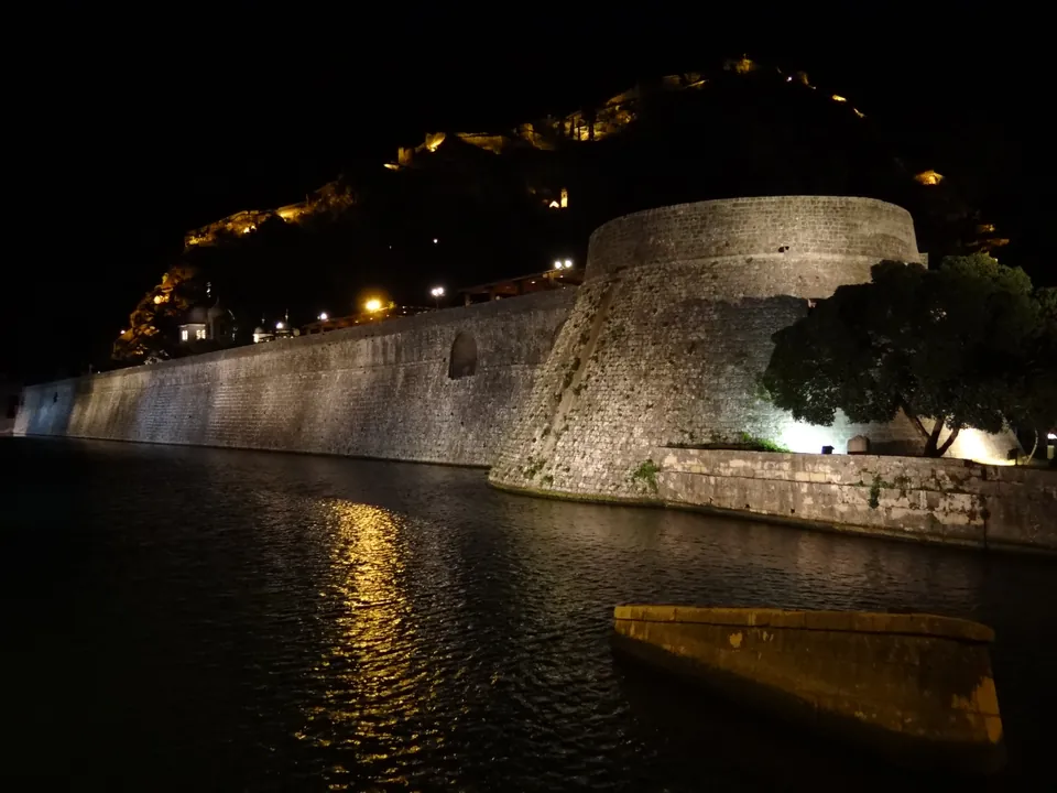 Illuminated city walls and fortress of Kotor reflected in the canal at night