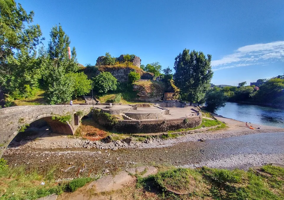 Stone arch bridge leading to the ruined Ribnica fortress on a riverbank in Podgorica