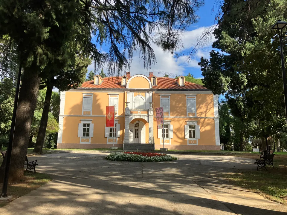 Ochre-yellow palace of King Nikola with a red-tiled roof framed by tall trees