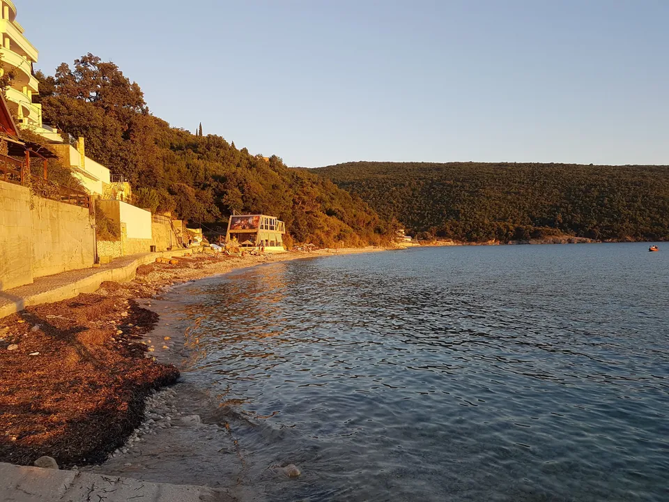 Kruče beach cove near Ulcinj lit by golden evening sunlight along the shoreline.