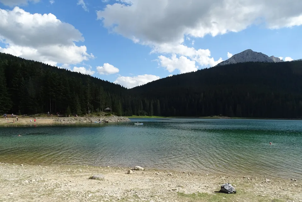 Bathers on the pebble shore of Black Lake with a rocky Durmitor peak behind