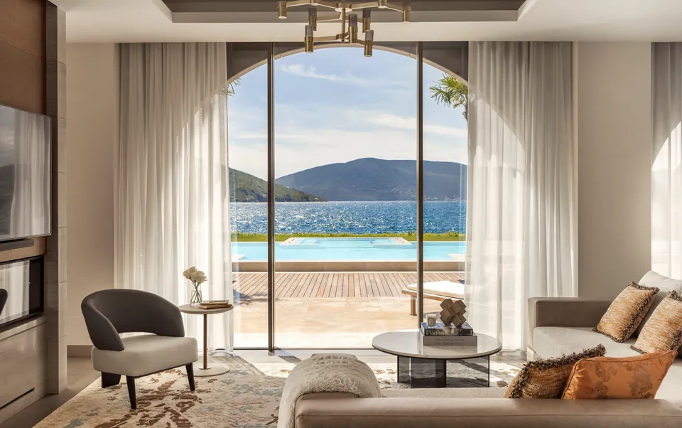 A villa living room opening through arched glass doors to a private pool and the bay