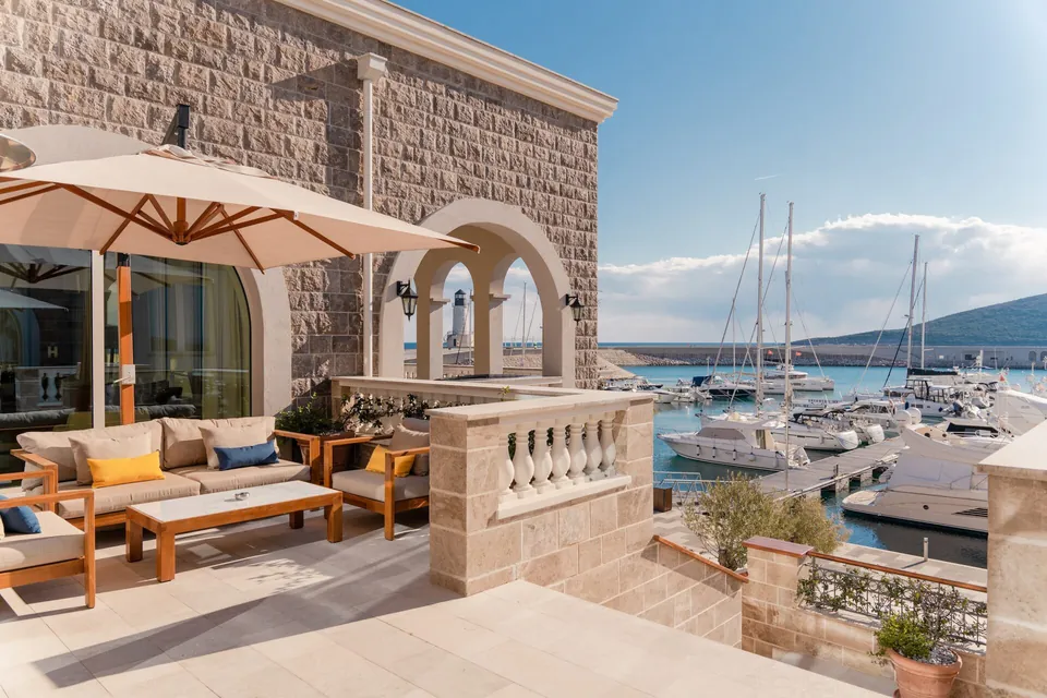 Terrace sofas with colourful cushions overlook yachts, lighthouse, hills and blue sky