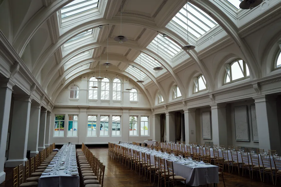 Long banquet tables in a hall with an arched glass roof