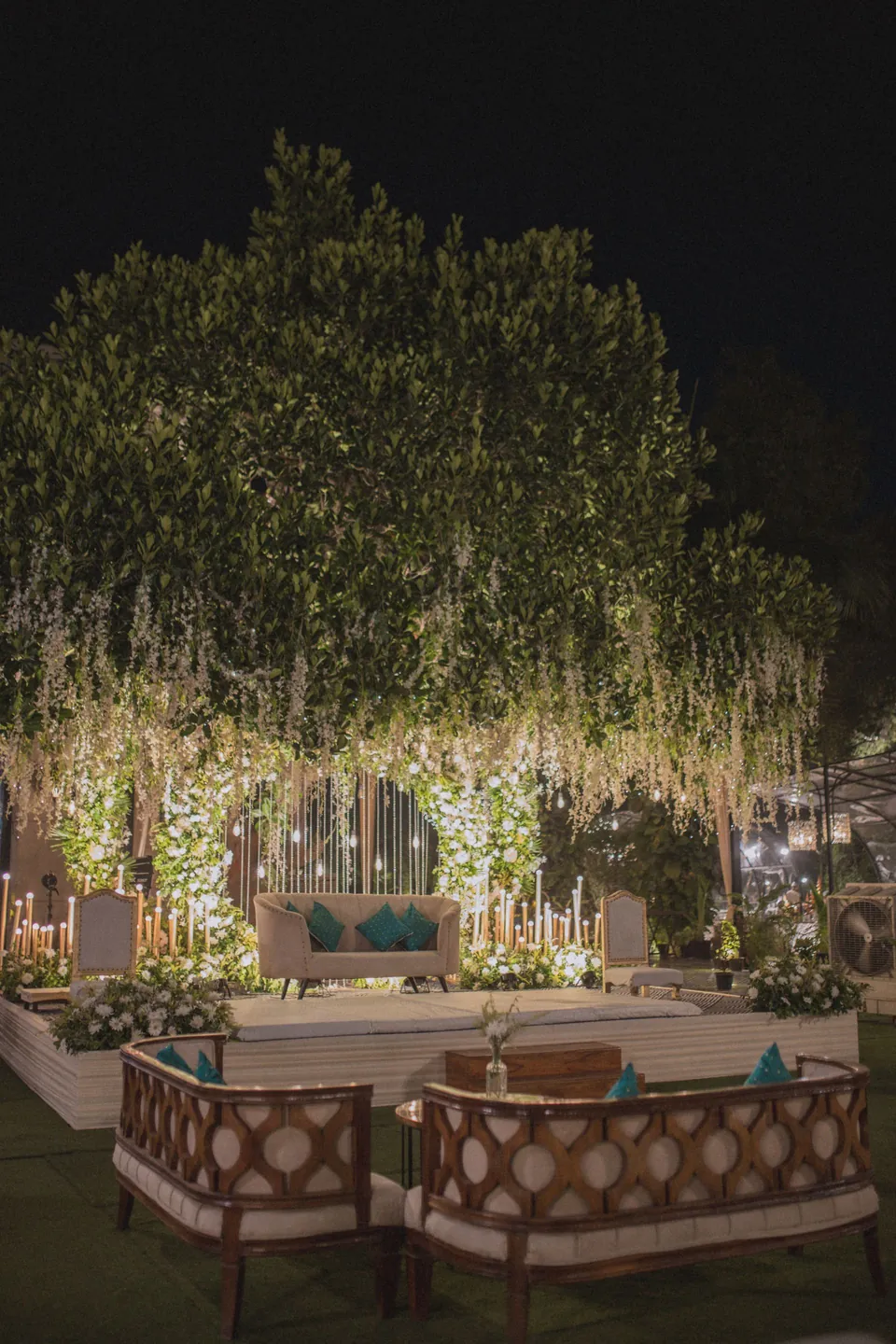 Evening lounge setting with a floral canopy and candle stands on a lawn