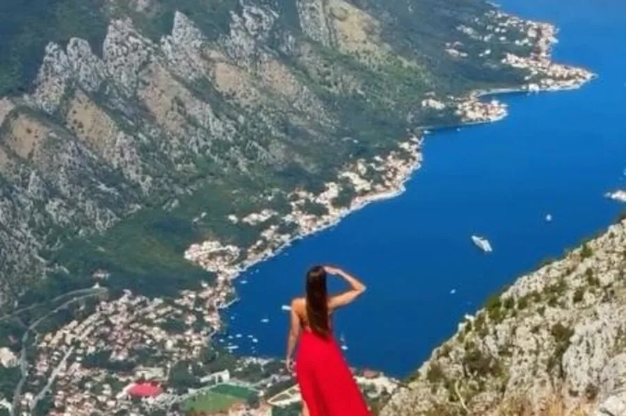 Woman in a red dress overlooking Kotor Bay, cliffs, shoreline settlements and yachts below