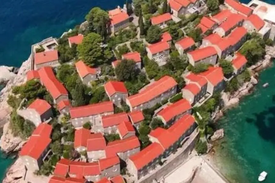 Aerial view of Sveti Stefan, red-roofed stone houses and turquoise sea.