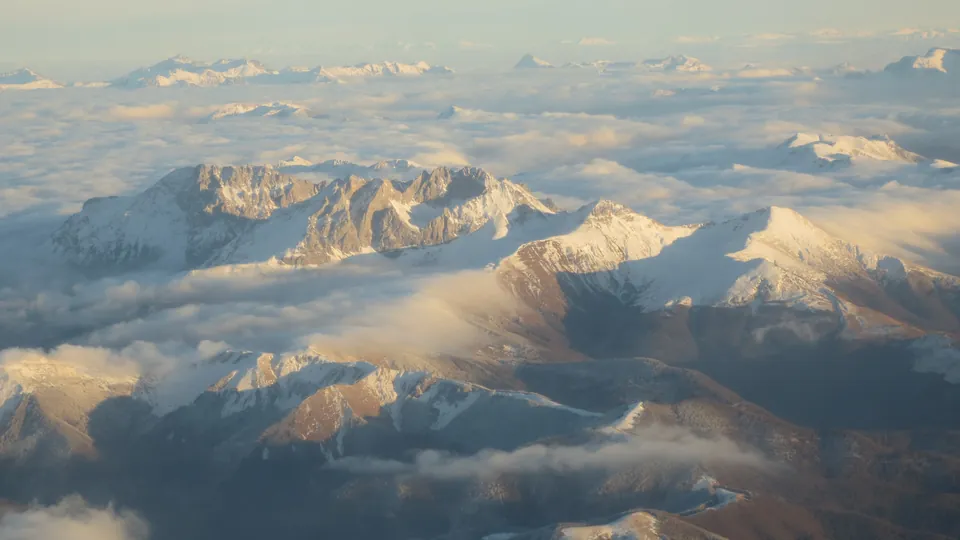 Snow-covered Komovi massif near Kolašin rises above clouds in warm winter sunlight.